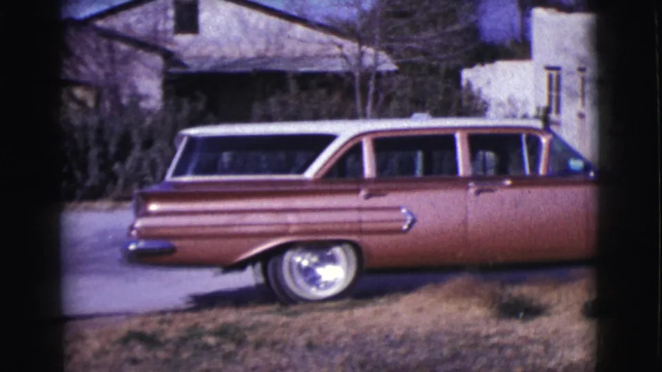 A reddish-brown station wagon with a light roof is seen near a driveway in 1961 Clarkdale residential footage.