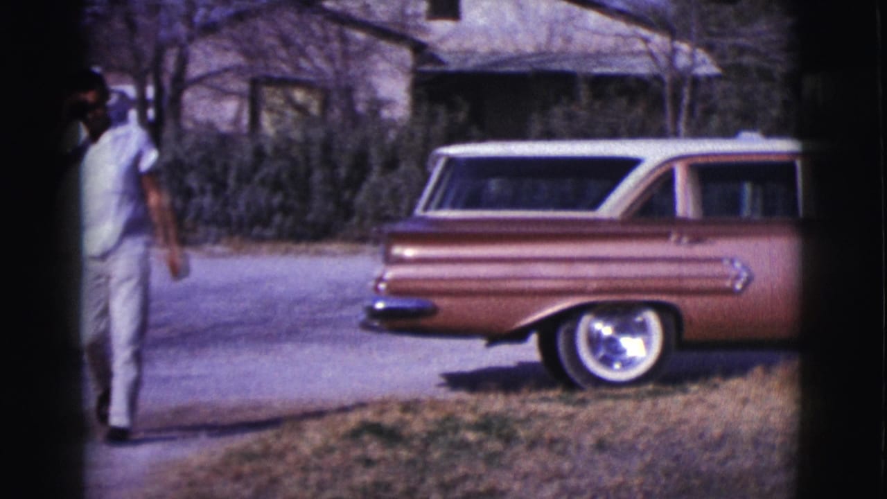 Man in light clothing near a copper station wagon on a sunny driveway.