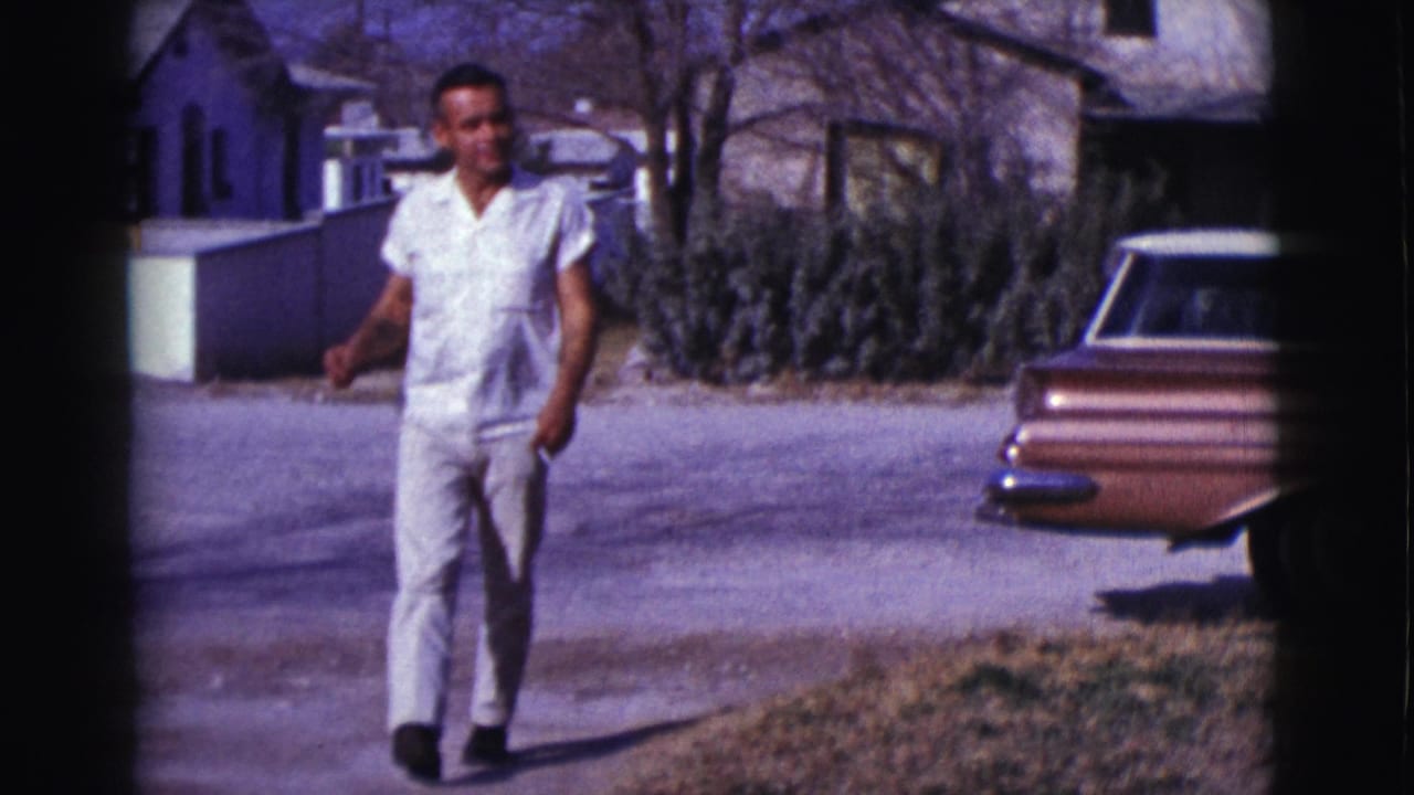 Man walks toward the camera beside a copper station wagon and houses.