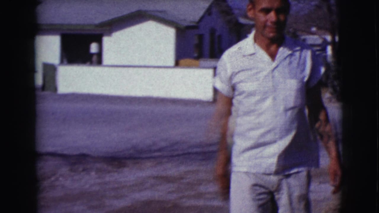 Man in a white short-sleeved shirt walks near low residential walls.