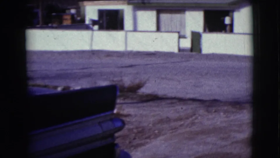 A dark mid-century car appears in the foreground with low walls and residential buildings in the Clarkdale, Arizona scene.