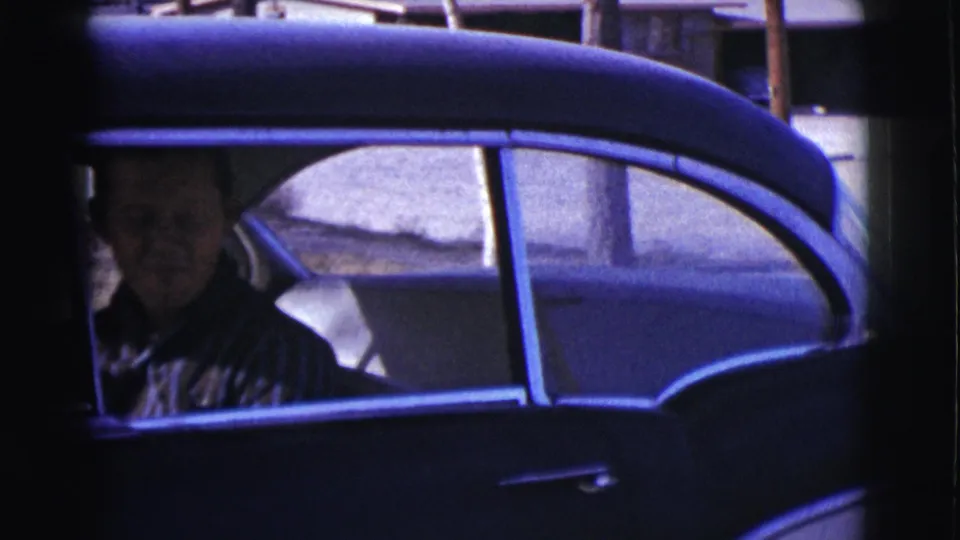 A woman is visible through the side window of a dark car in this 1961 Clarkdale, Arizona home-movie frame.