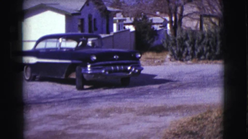 The car turns or backs into the street, showing its side and rear near Clarkdale houses, fencing, shrubs, and bare trees.