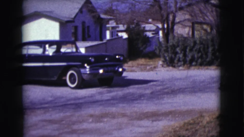 A black-and-white car with whitewall tires moves farther through the Clarkdale street scene, framed by modest houses and winter-bare trees.