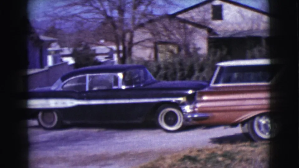 The black-and-white car passes a brown station wagon in a Clarkdale neighborhood, with houses and shrubs visible in the background.