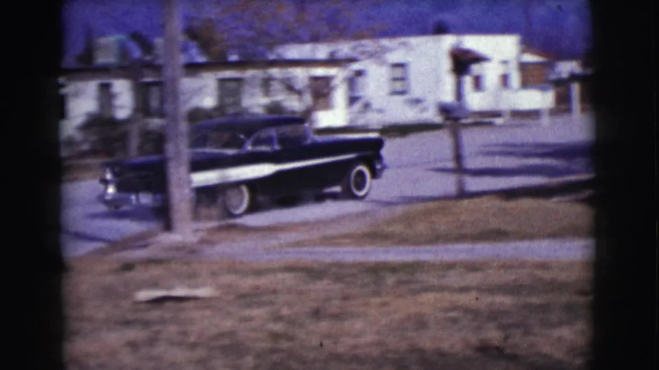Home-movie view of a black sedan along a Clarkdale residential street, partly blocked by a foreground tree.