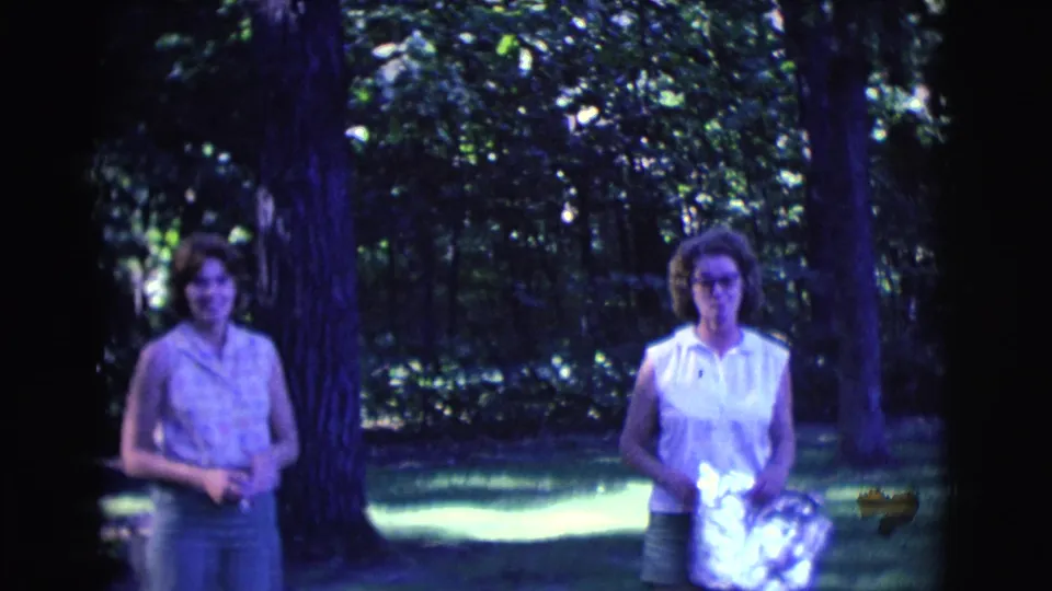 Two young women stand near a large tree in 1961 Clarkdale, Arizona, framed by dark foliage and bright grass.