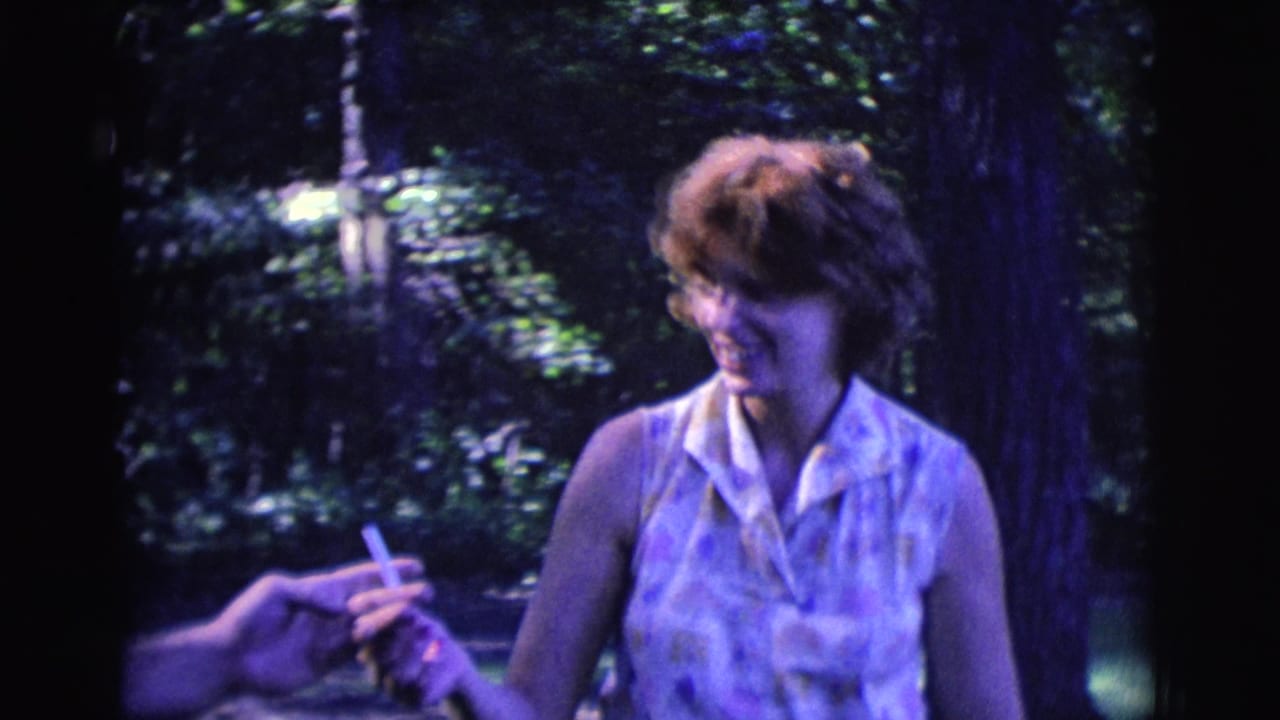 Woman smiles as a hand reaches toward the cigarette she is holding outdoors.