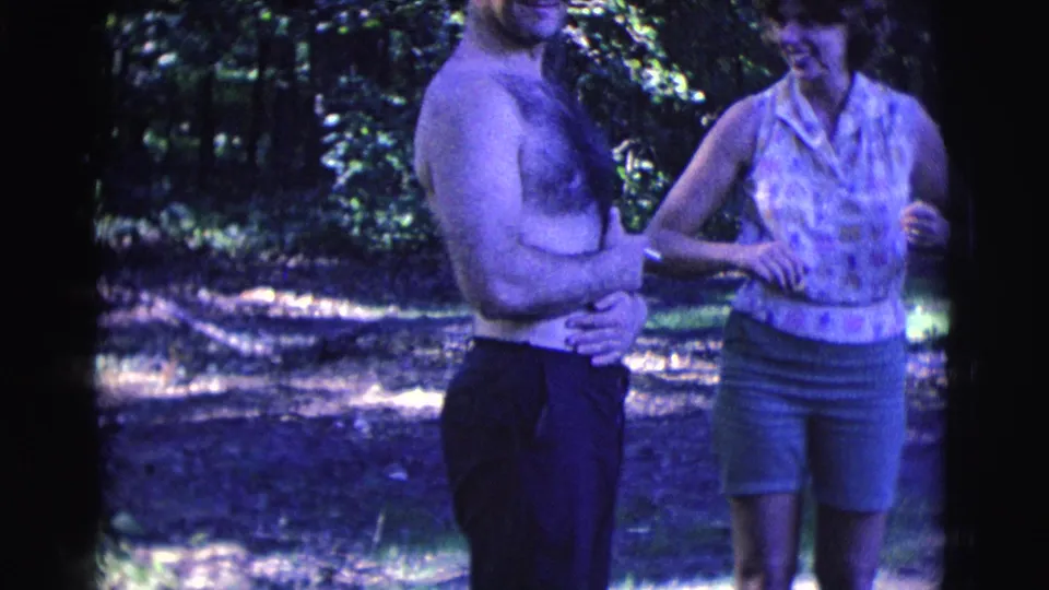 The woman stands close to the shirtless man and gestures toward his arm in a playful Clarkdale, Arizona 1961 home-movie moment.