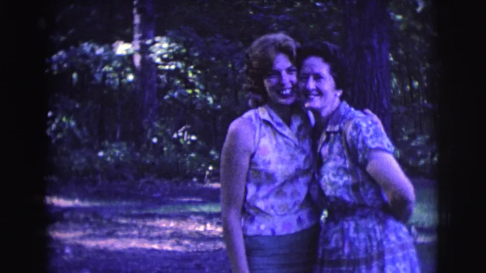 Two adult women stand arm in arm and smile in a wooded garden setting in Clarkdale, Arizona, 1961.