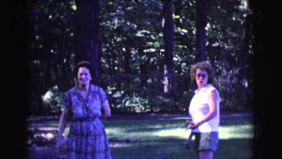 In metadata-supported 1961 Clarkdale, Arizona footage, two adult women face the camera in a wooded park, one in a patterned dress and one in a white sleeveless top.