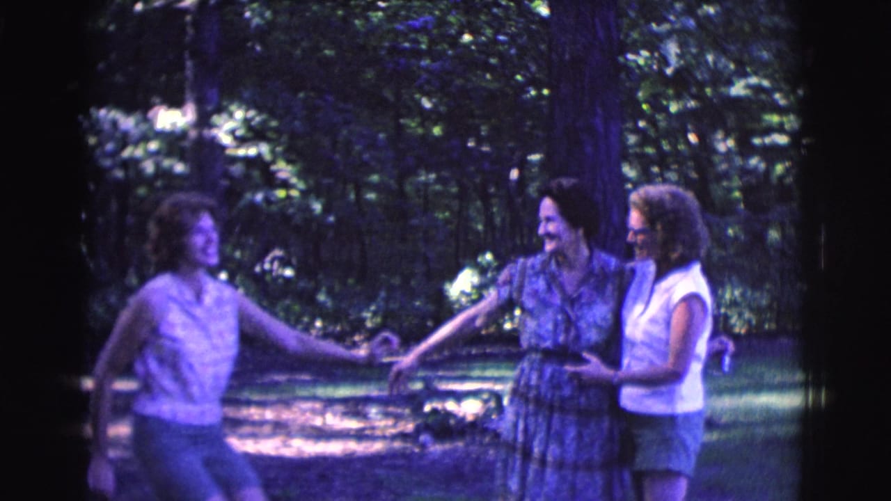 Three adult women hold hands and laugh in a shaded outdoor clearing.