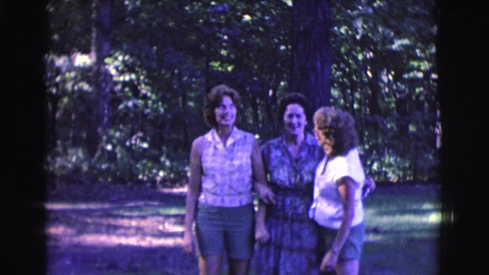 Three adult women smile together beneath trees in this 1961 Clarkdale, Arizona 8mm home-movie frame.