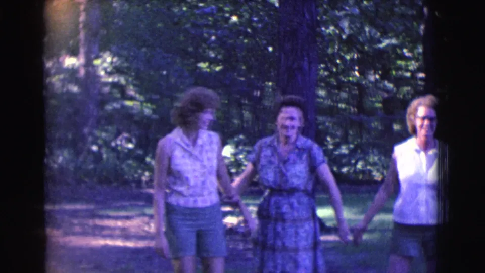 Three adult women walk arm-in-arm through a wooded Clarkdale path in 1961 8mm home-movie footage.