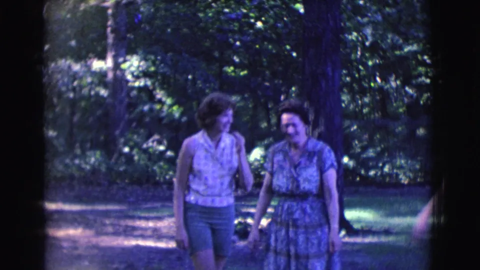 Two of the women move along the shaded forest path, with soft 8mm color and visible tree cover around them.