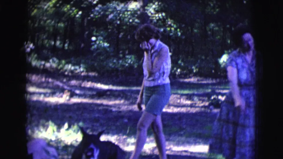 A woman in shorts walks near a small dark dog on the forest path, with the rest of the group partly visible behind her.