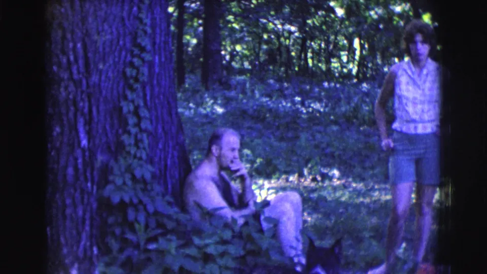 1961 Clarkdale, Arizona home-movie frame of a seated man by a large tree with a woman standing in the woods.