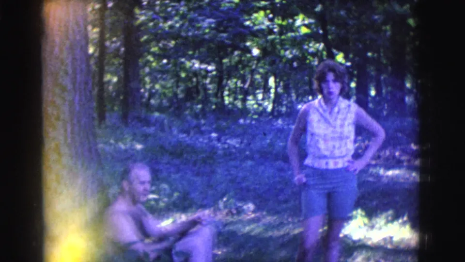 1961 Clarkdale, Arizona frame showing a woman standing with hands on hips while a man sits partly in shade nearby.