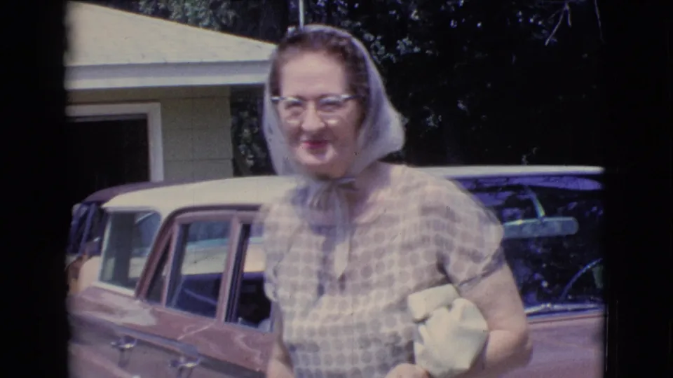 The final frame shows the woman close to the camera, smiling in front of the car and house exterior during the 1961 Clarkdale, Arizona home-movie scene.
