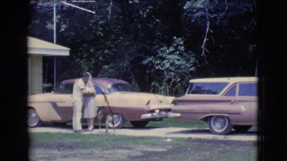 1961 Clarkdale, Arizona frame with an adult couple standing close near a dog between two two-tone parked cars.