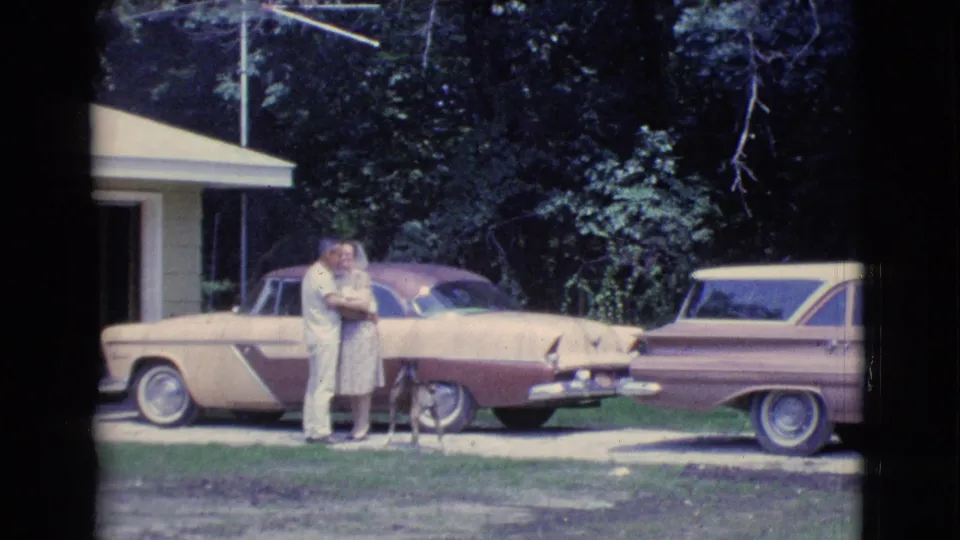 1961 Clarkdale, Arizona home-movie frame showing a couple embracing near a small dog and parked two-tone cars.