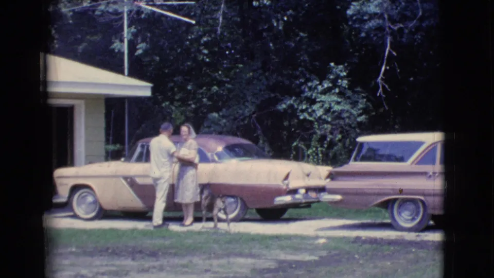 1961 Clarkdale, Arizona frame of a man and woman standing together with a dog near two parked two-tone cars.