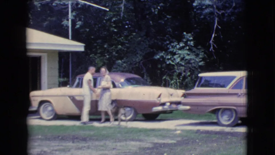 In Clarkdale, Arizona in 1961, a couple stands by a two-tone sedan as a dog waits nearby in a residential driveway.