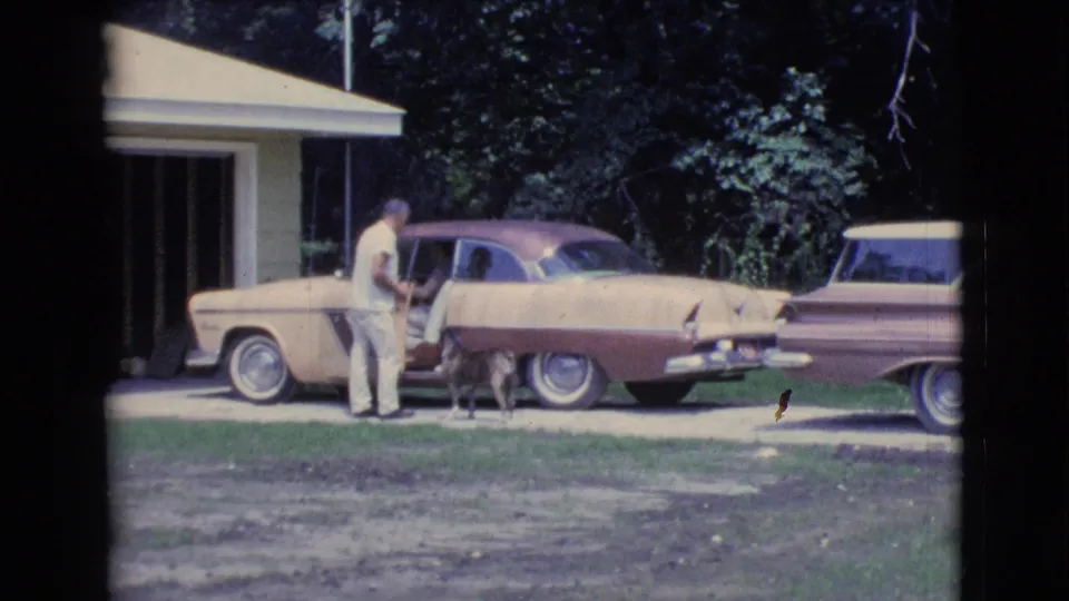 1961 Clarkdale, Arizona frame of a driveway conversation beside a two-tone sedan, with a small dog near the car door.