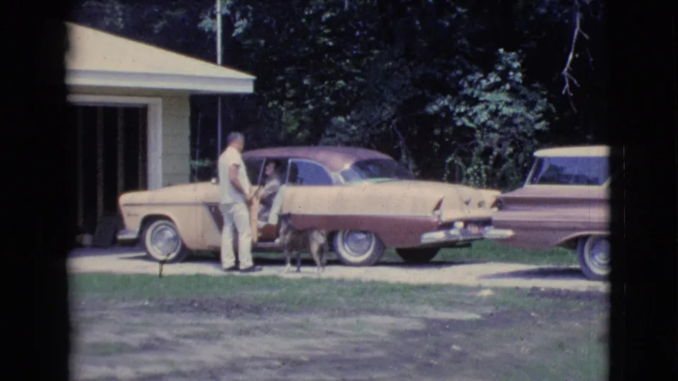 Clarkdale, Arizona 1961 home-movie still with a man, passenger, dog, two vintage cars, and a house driveway setting.