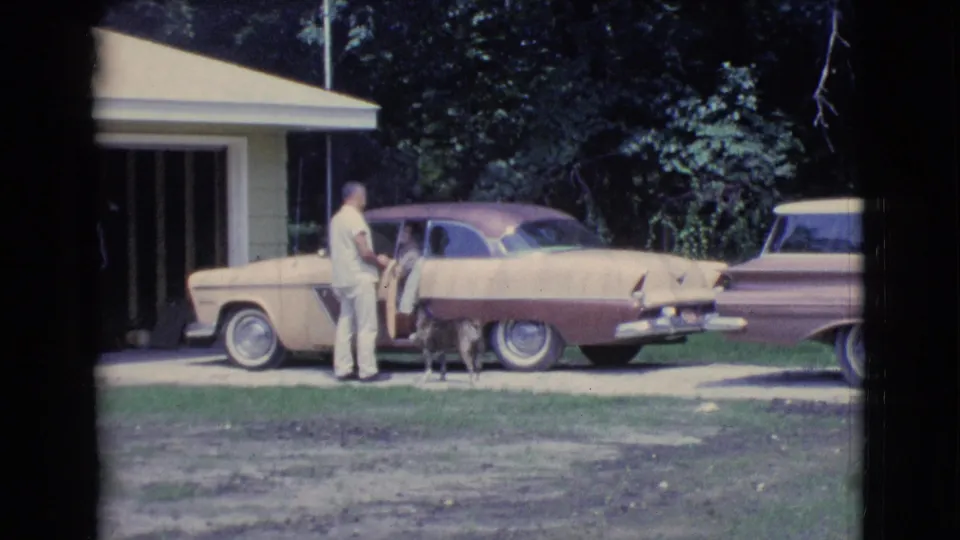 1961 Clarkdale, Arizona home-movie frame of a man beside a two-tone car in a driveway, with a dog near the door.