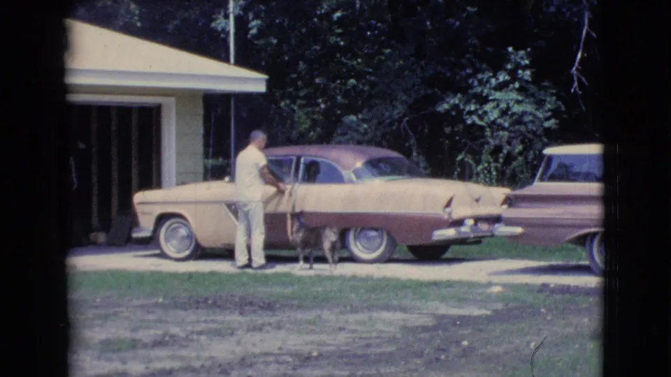 1961 Clarkdale, Arizona frame showing a man and dog beside a parked two-tone car outside a garage.