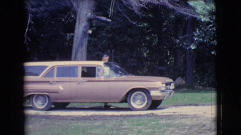 A two-tone station wagon remains parked in the Clarkdale driveway, with a person visible near the front window area against a wooded yard.