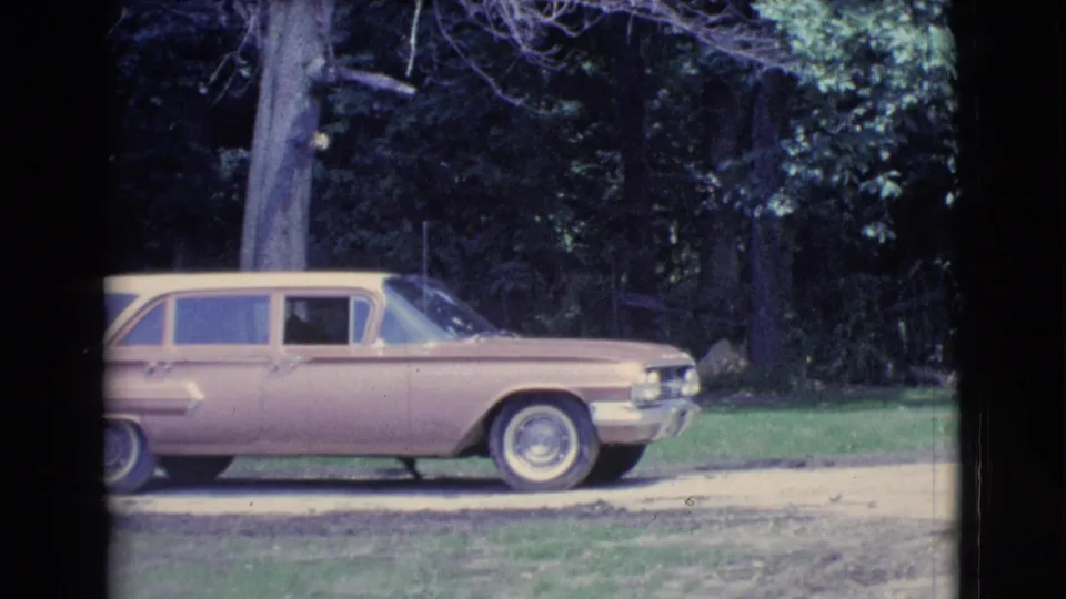 1961 Clarkdale, Arizona home-movie frame showing a cream and maroon car on a driveway near trees and grass.