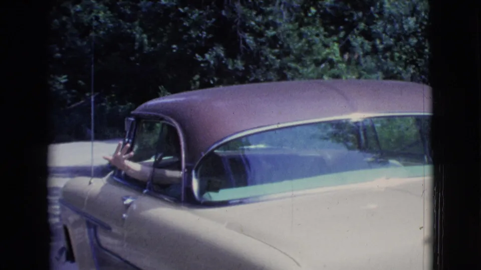 Close 1961 Clarkdale frame of the two-tone sedan as the driver waves from the side window toward the camera.
