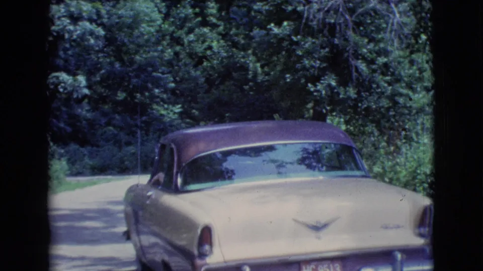 Final 1961 Clarkdale frame showing the sedan from the rear as it moves away beside dense greenery.