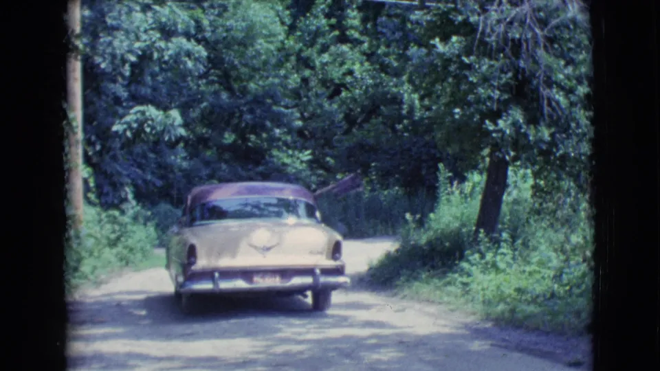 The two-tone sedan continues away along a narrow wooded road, matching the supplied 1961 Clarkdale, Arizona home-movie context.