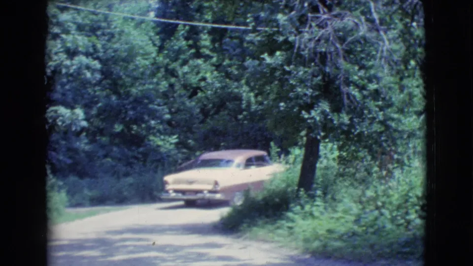 The two-tone car continues through a wooded Clarkdale roadside scene, partly framed by 8mm film borders.