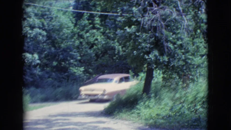 The car slows near thick green brush on the wooded roadside in the 1961 Clarkdale home-movie scene.