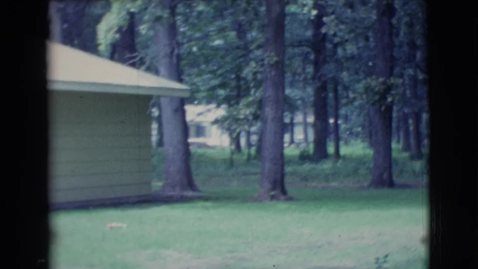 The pan reaches a light-sided house or garage in a wooded Clarkdale yard, with grass and tall trees around it.