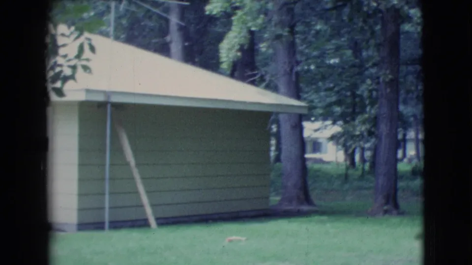 1961 home-movie view of a light-sided residential exterior with a sloped roof, lawn, and trees in Clarkdale, Arizona.