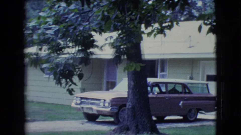 1961 Clarkdale, Arizona frame with the brown station wagon more centered beside the yellow house, partially obscured by a large tree.