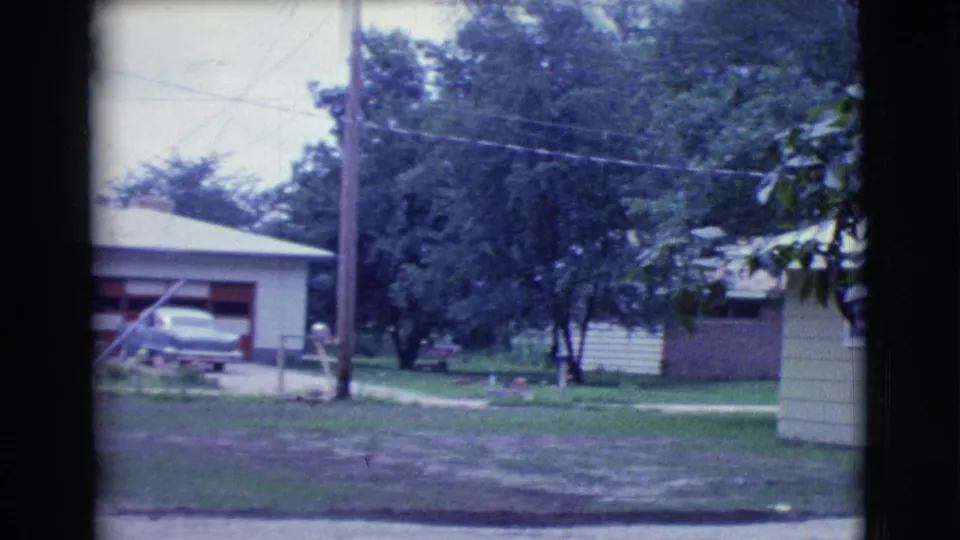 1961 Clarkdale, Arizona frame looking across a quiet residential yard with a utility pole, trees, neighboring garage, and partial yellow house.