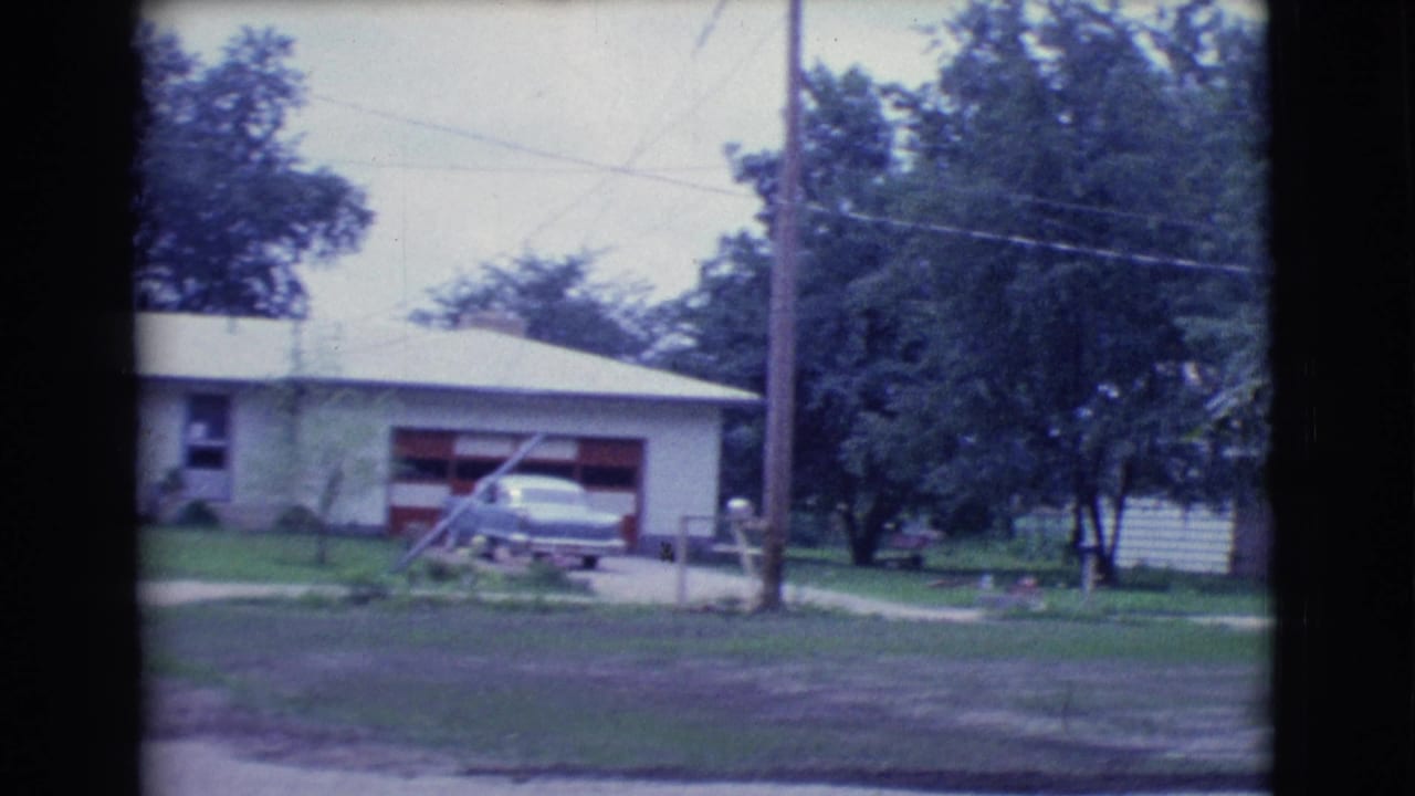 Single-story house with red garage door, parked sedan, driveway, lawn, trees, and utility pole.