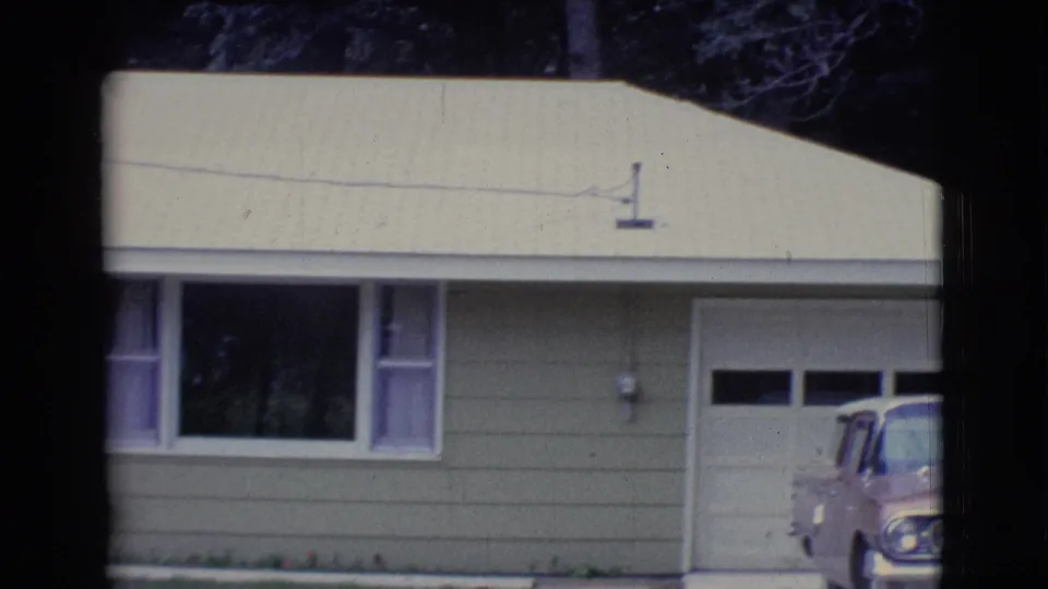 Clarkdale, Arizona home-movie frame showing a yellow ranch house facade, front windows, garage door, and part of a parked sedan.