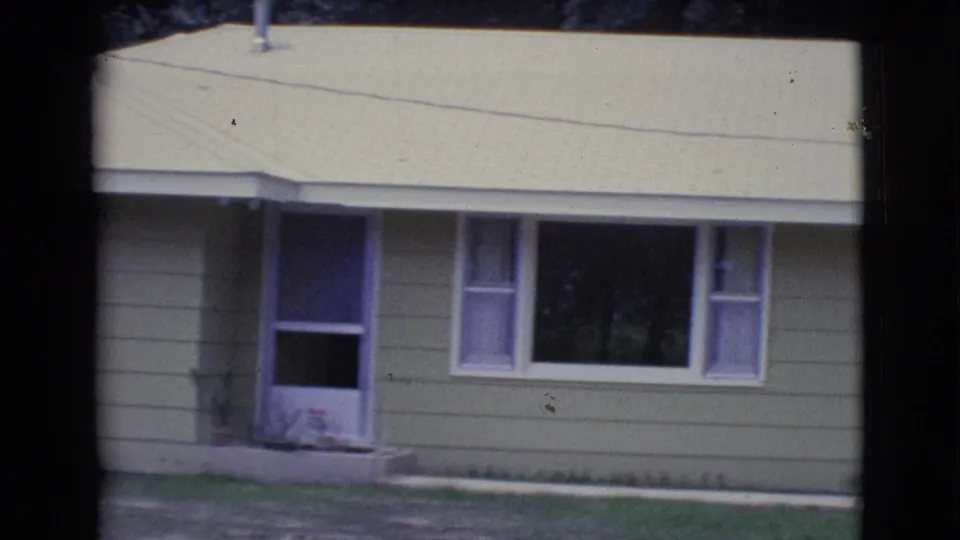 1961 Clarkdale frame showing the front entry, picture window, pale roofline, and lawn of a yellow ranch-style house.