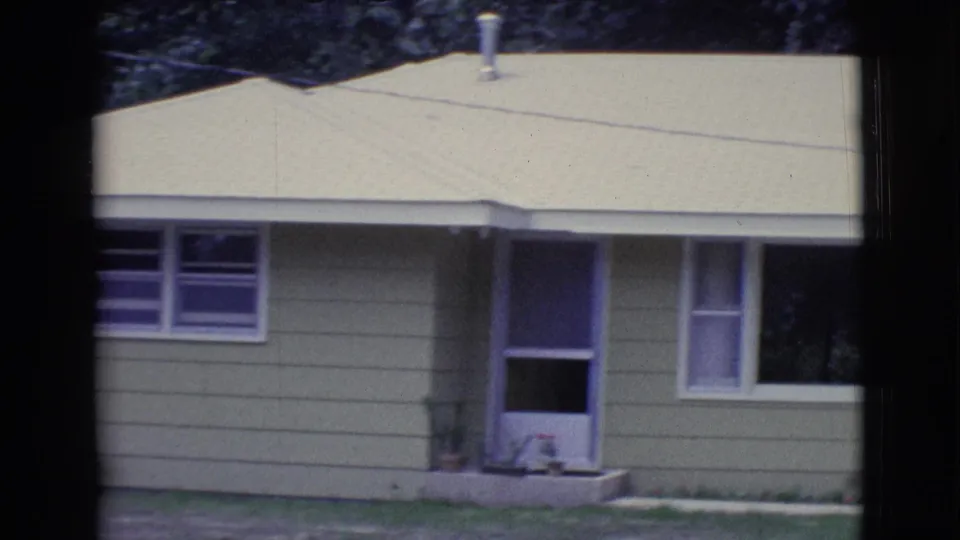 1961 Clarkdale, Arizona 8mm frame showing the front corner of a green house with porch opening, windows, and pale roof.