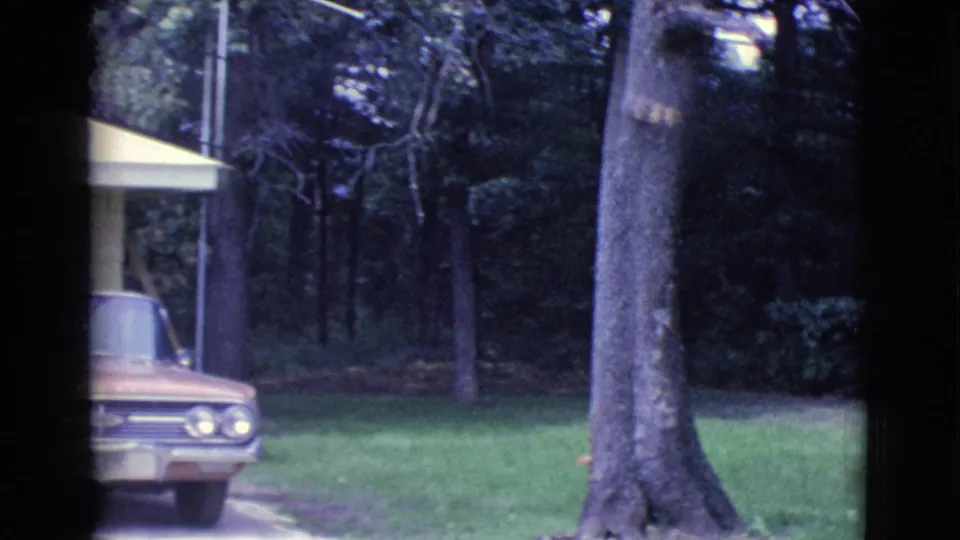 1961 Clarkdale, Arizona home-movie frame showing the car and house edge beside a lawn and mature trees.