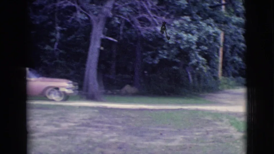 1961 Clarkdale home-movie frame showing trees, grass, a dirt path, and the rear portion of a pink station wagon.