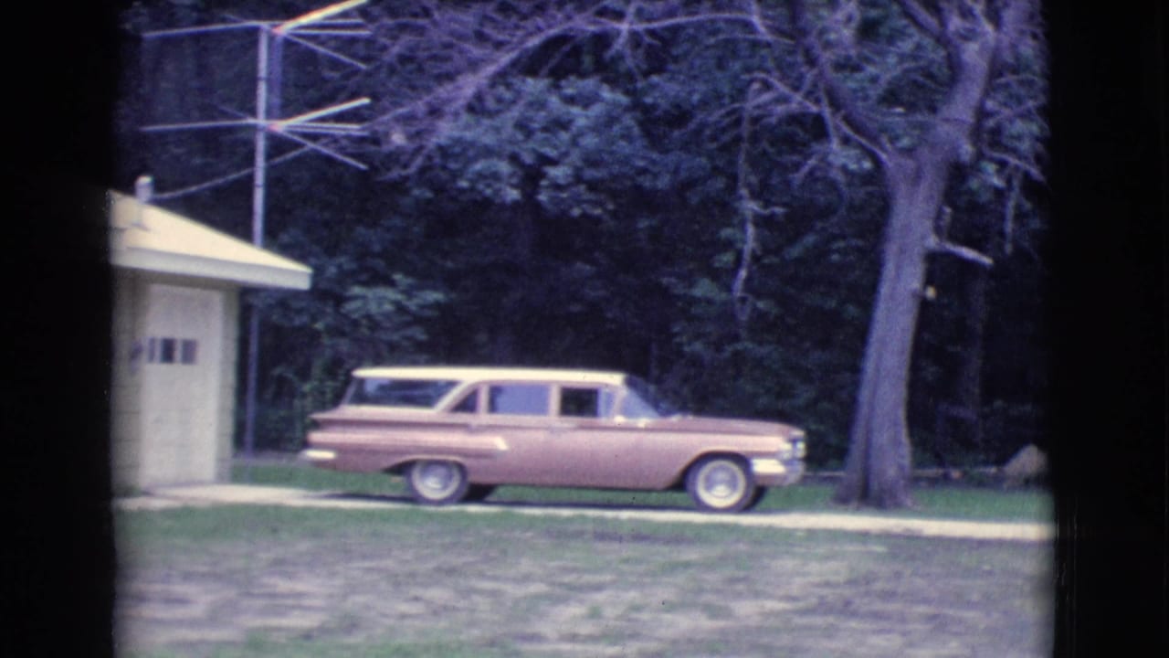 Pink station wagon parked beside a small yellow house and garage.