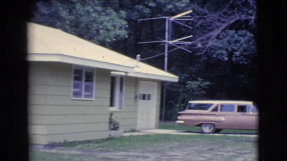 1961 Clarkdale home exterior showing yellow siding, windows, garage, outdoor antenna, lawn, trees, and a parked station wagon.